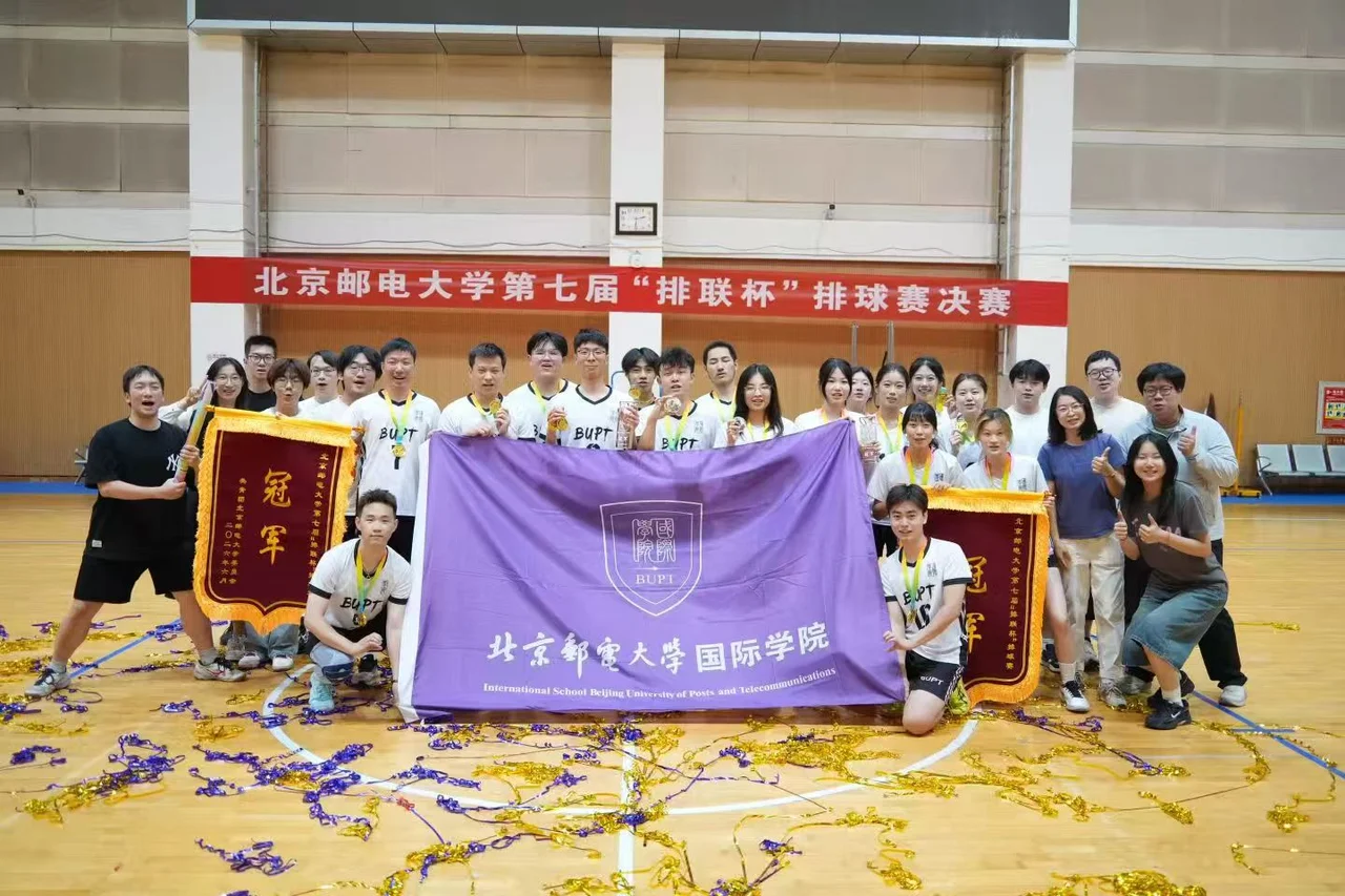 国际学院队员和伙伴在赛场合影，举着紫色院旗和两面写有冠军的锦旗，胸前挂着奖牌
