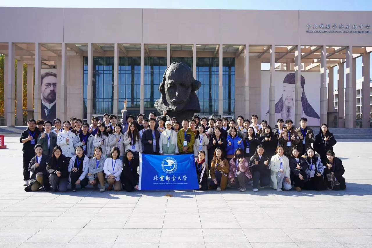 剧组在中央戏剧学院剧场中心前合影,前排展开北京邮电大学校旗
