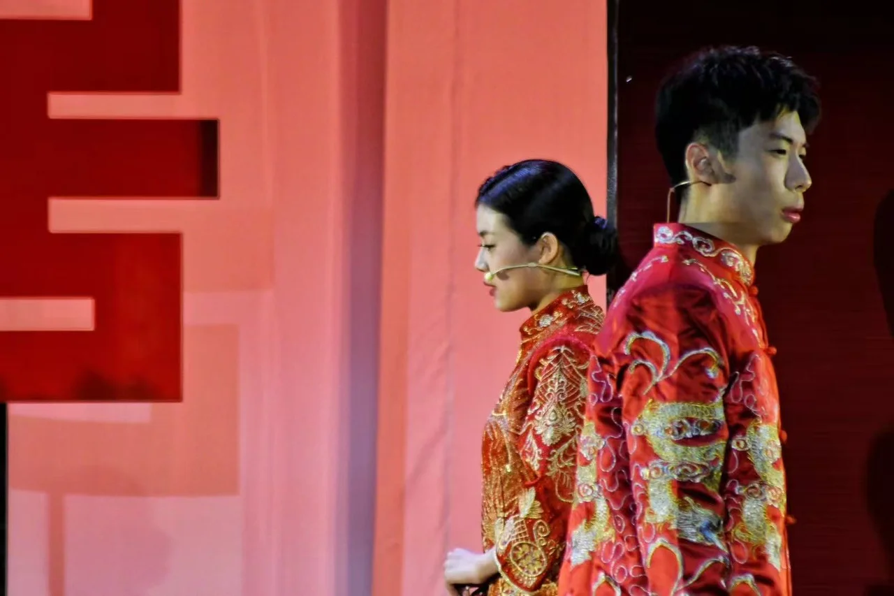 两位身穿红色婚服的演员背对背站在红色舞台布景前
