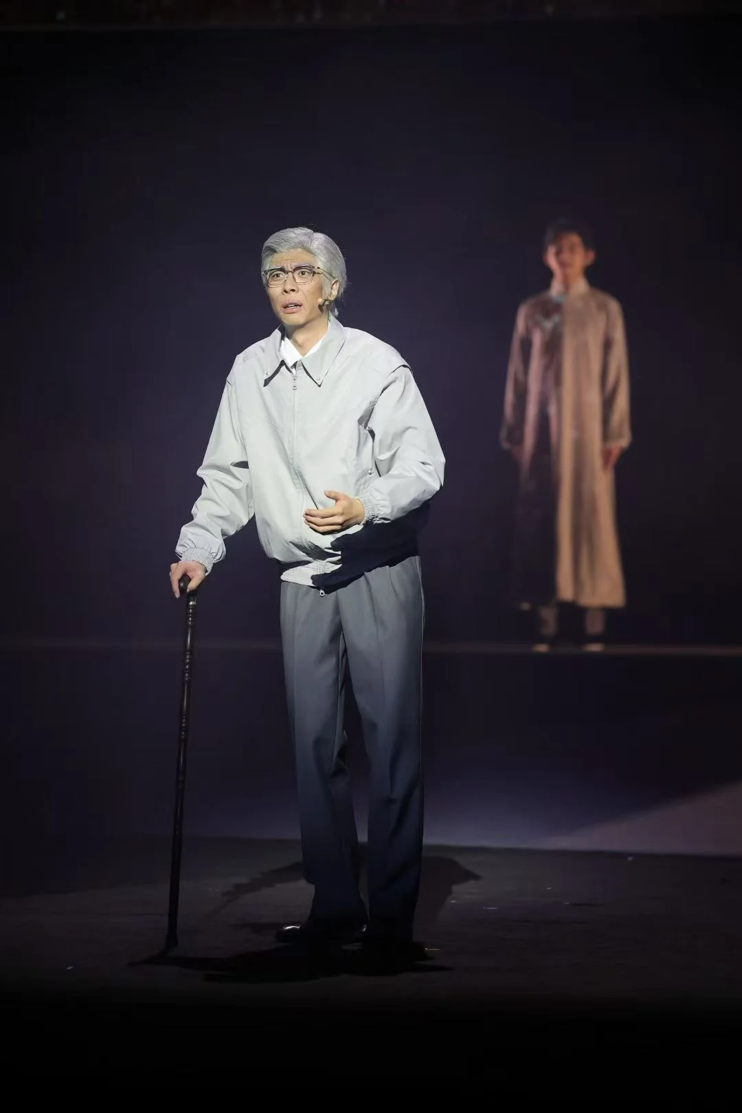 《与光同行》舞台上,灰发演员戴着眼镜、拄着手杖,后方还有一位演员