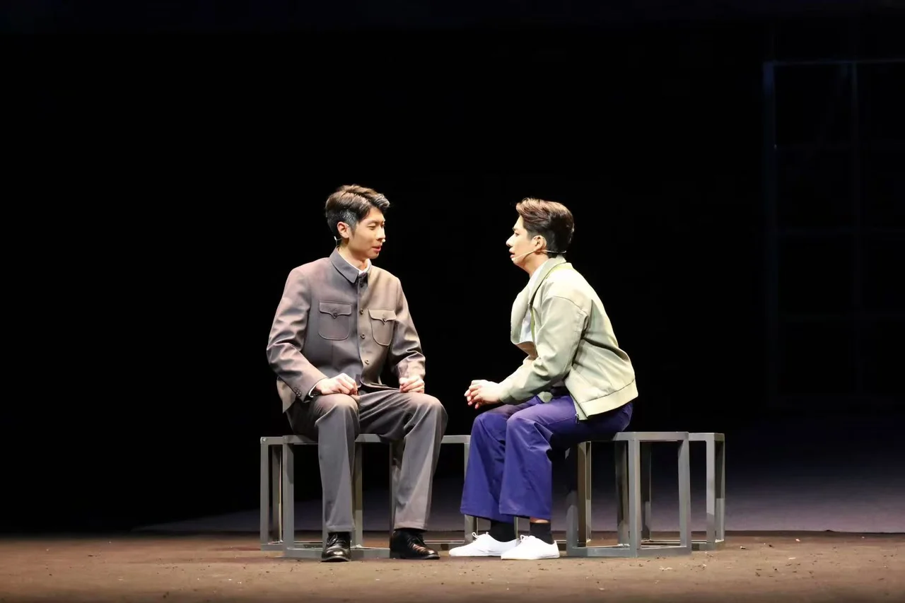 《与光同行》舞台上,两位演员面对面坐在方凳上交谈