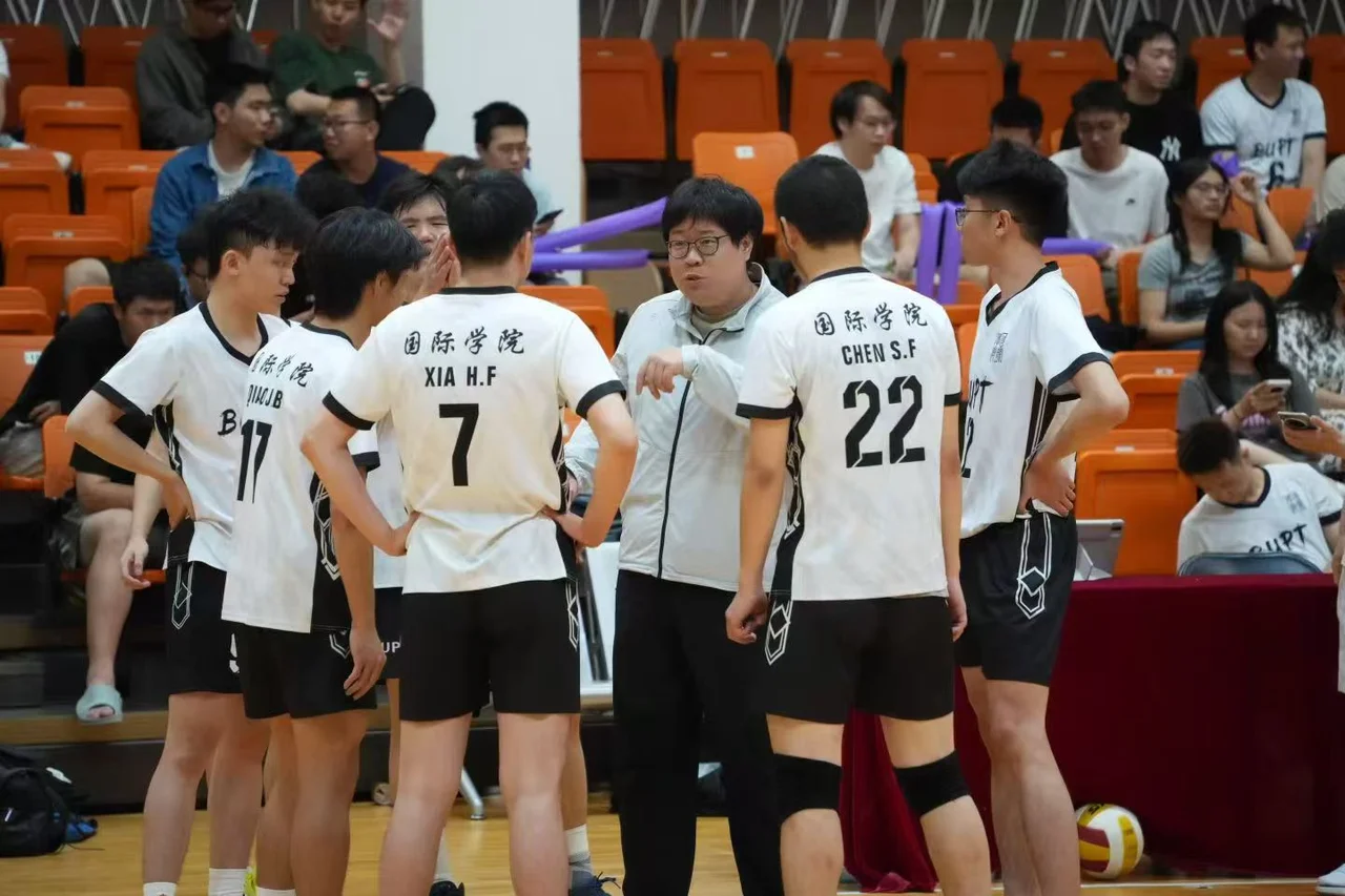 国际学院排球队队员身穿白色球衣，在场边围着一位身穿浅色外套的人交流